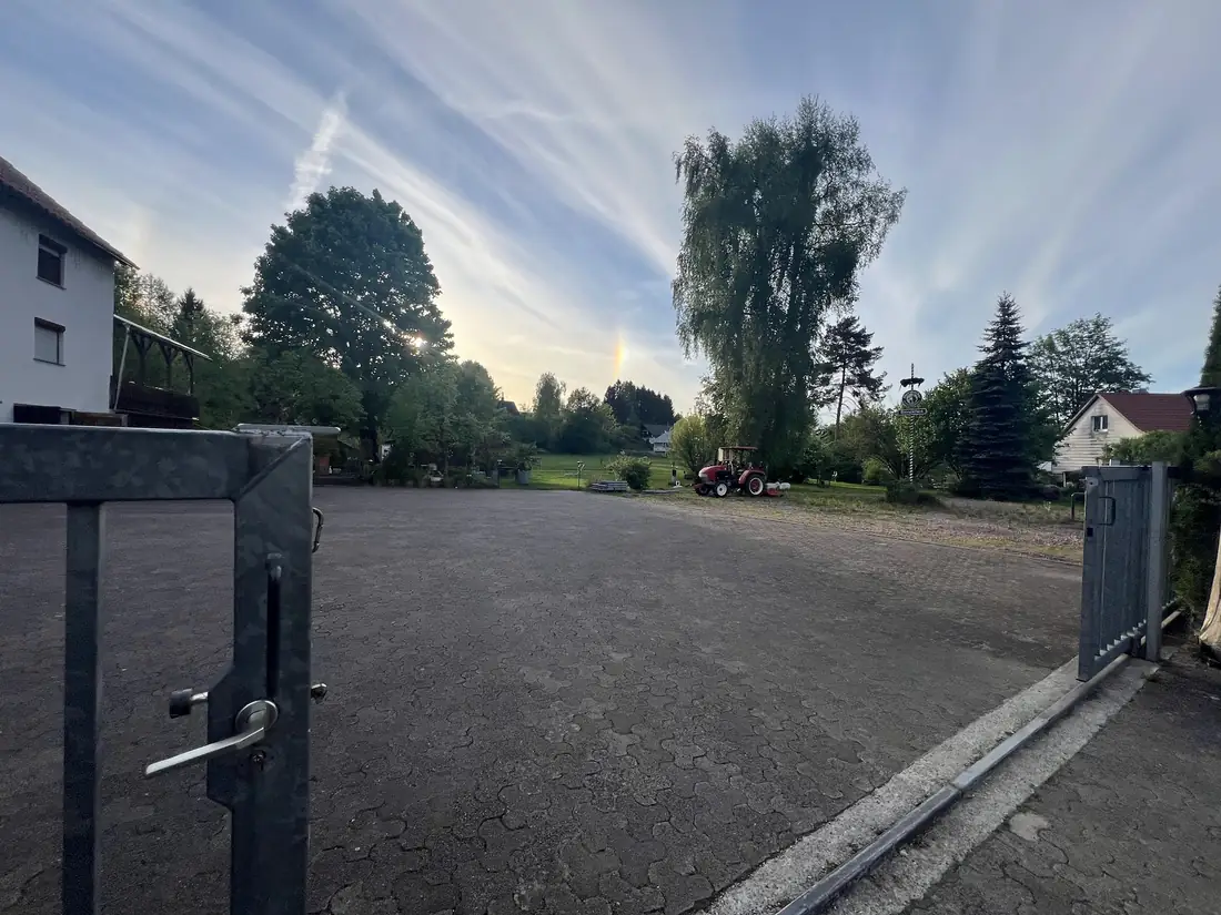 Blick durch das geöffnete Tor auf den befestigten Parkplatz